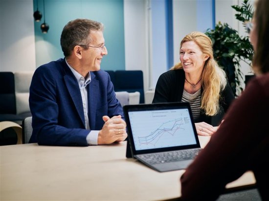 Mann og dame sitter ved et bord og smiler bak en laptop som viser et diagram